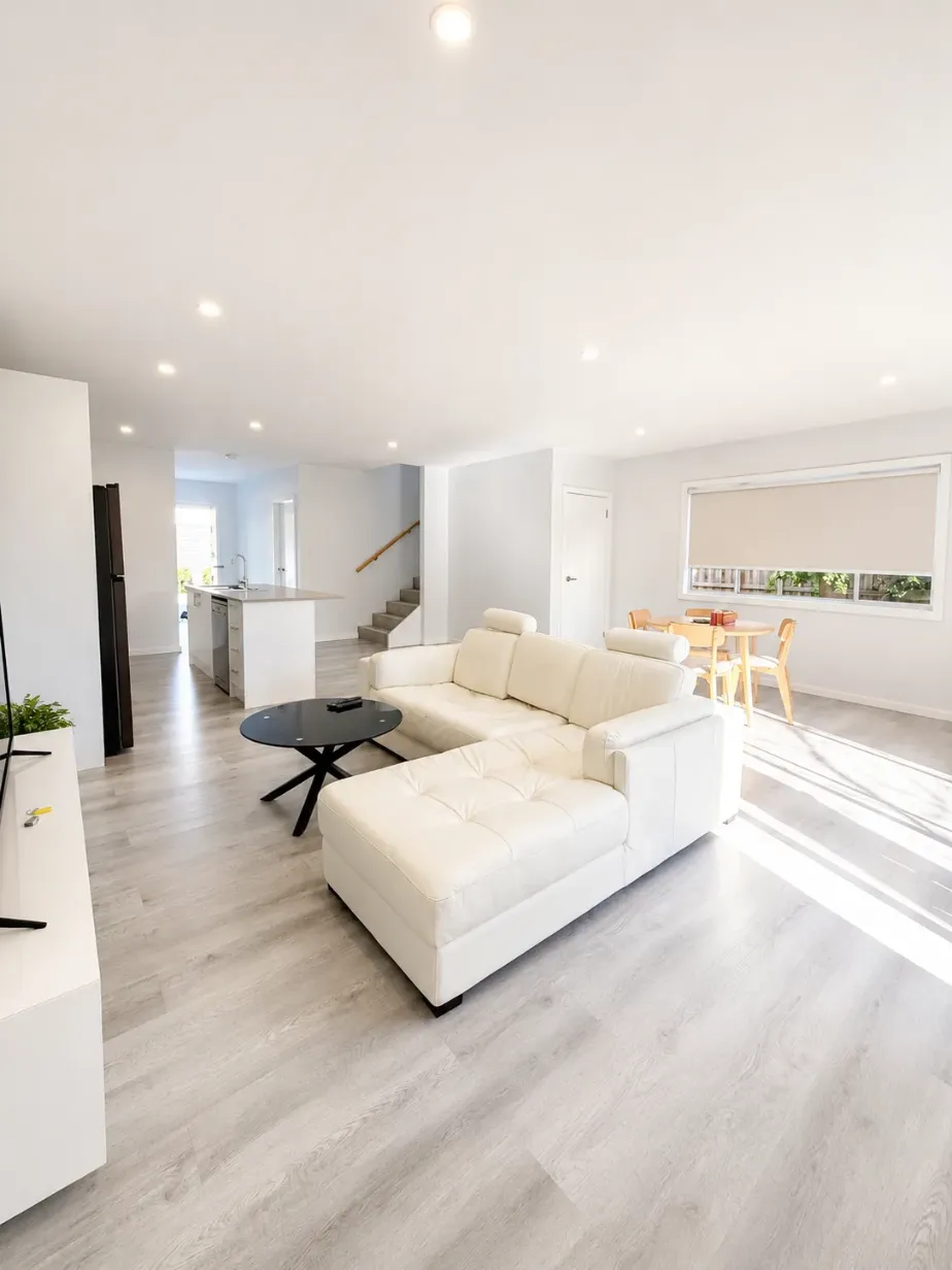 Open-plan living and dining area with white leather sofa, timber-look floors and staircase