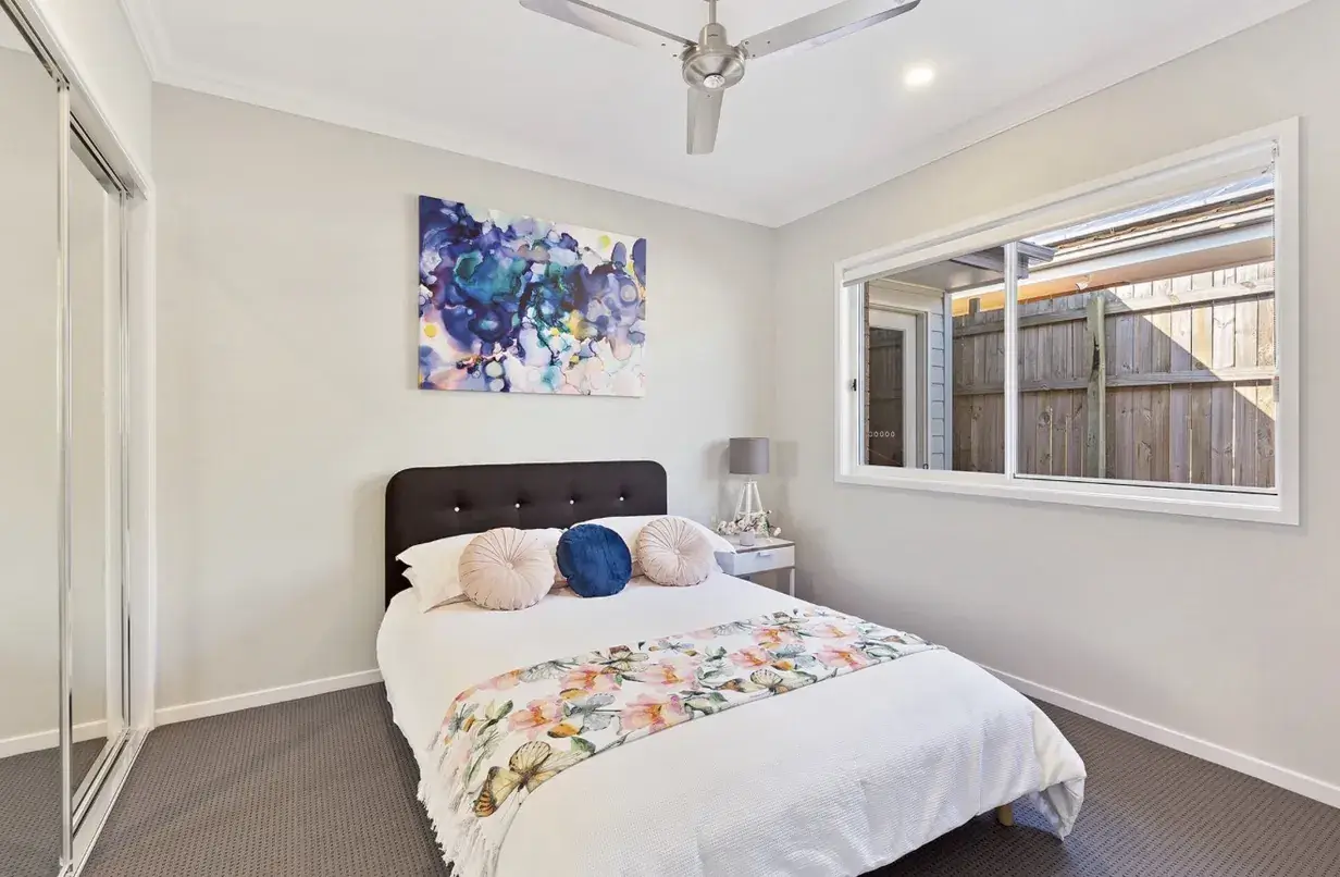 Carpeted bedroom with dark upholstered bedhead, floral throw and ceiling fan