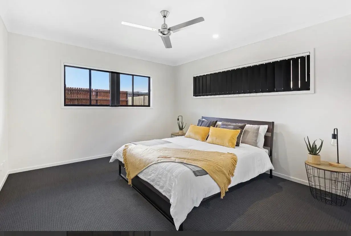 Carpeted bedroom with dark bedhead, mustard cushions and ceiling fan